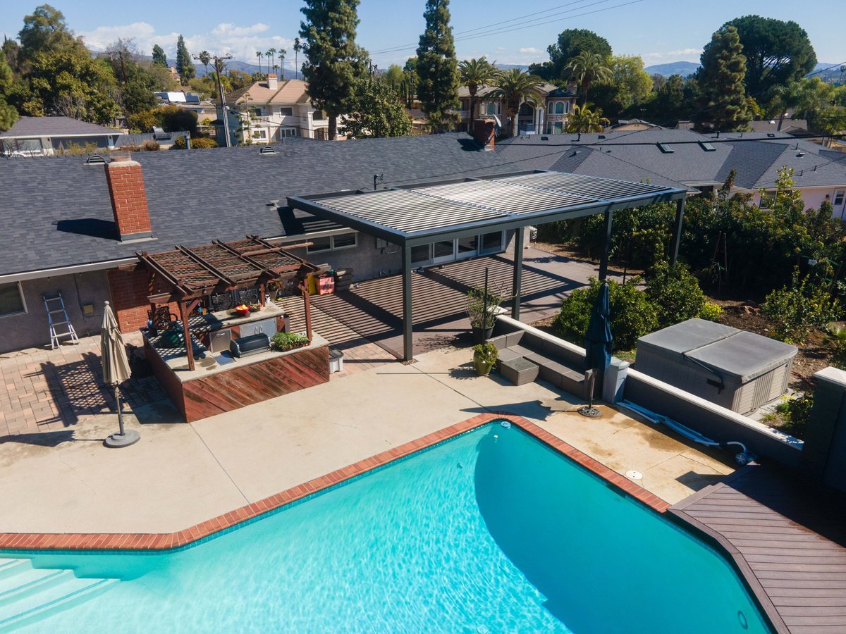 Backyard with turquoise swimming pool, patio, and pergola overlooking residential neighborhood with mountains in background