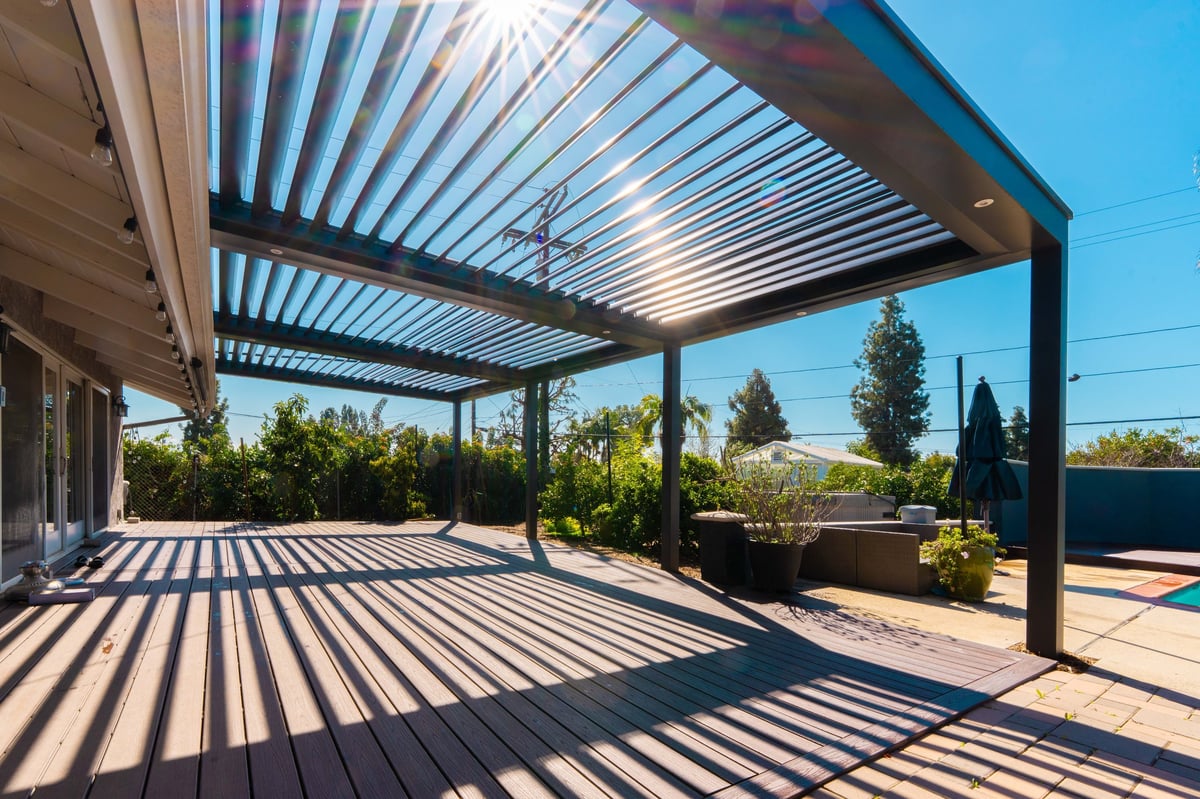Modern pergola with louvered aluminum roof over a spacious patio deck with striped shadows and landscaped surroundings