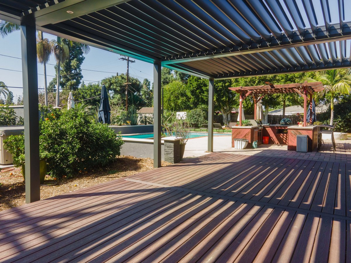 Modern patio with pergola shade structure overlooking a backyard pool and landscaped garden area