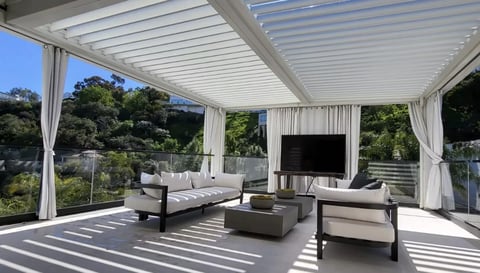 Modern outdoor patio with retractable pergola, contemporary furniture, mounted TV, and panoramic garden views